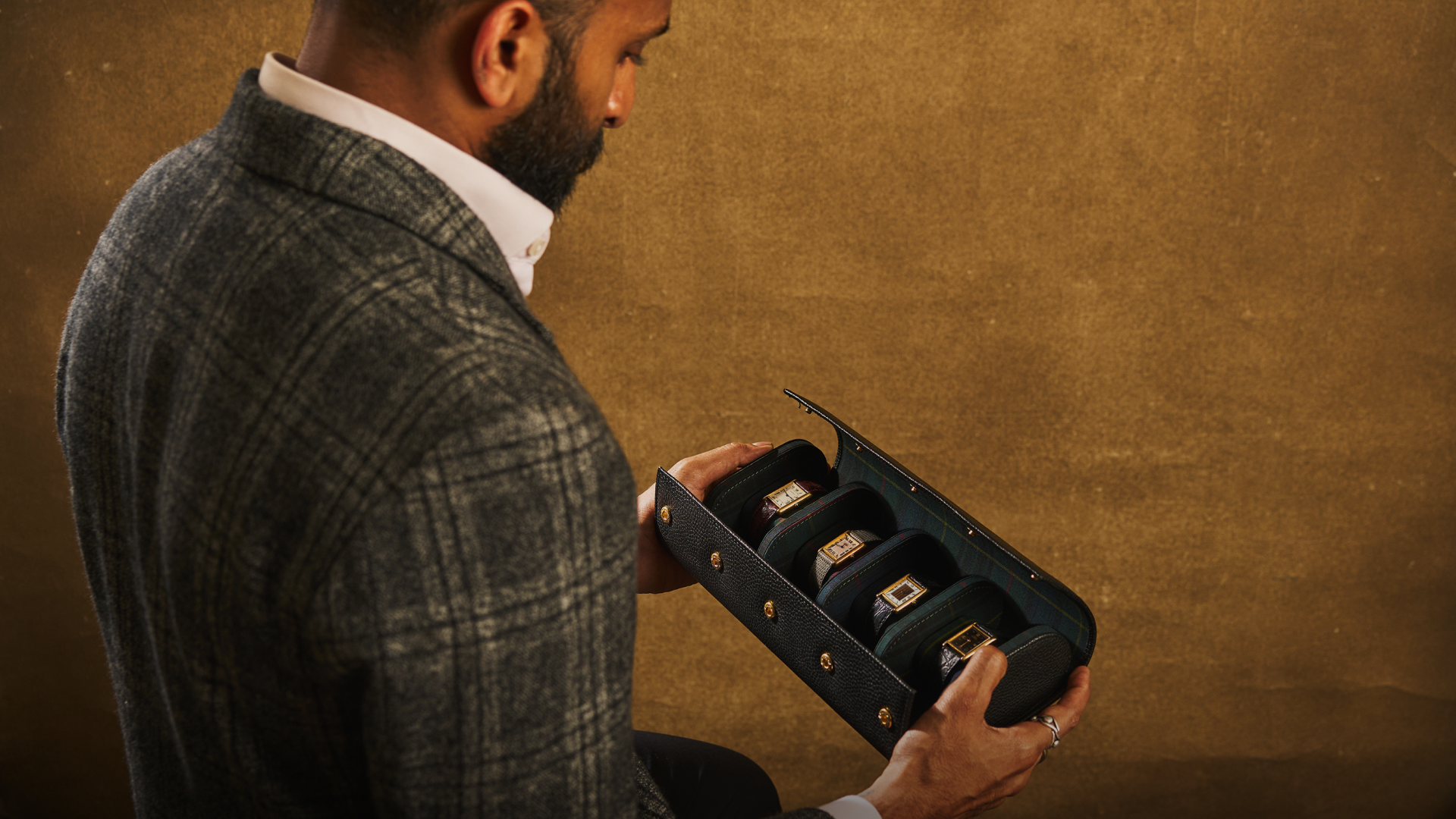 Man in a suit holding an open black jewelry box with rings on a brown background