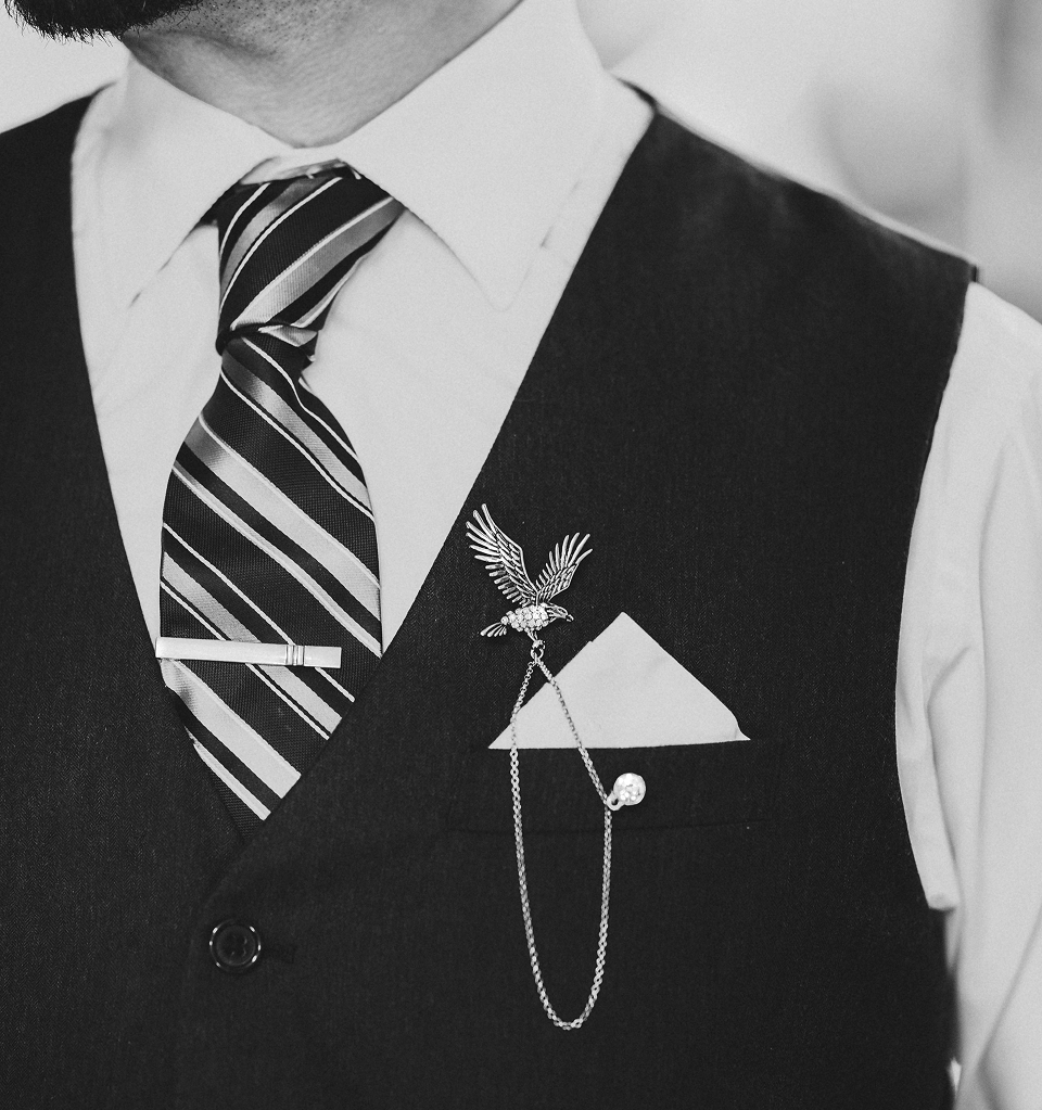 Man wearing a black vest with an eagle brooch and striped tie.