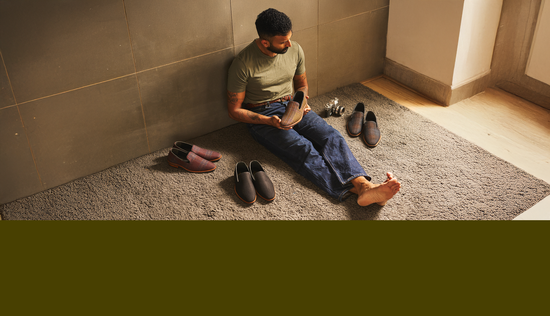 Man sitting on a rug with shoes around him in a room.