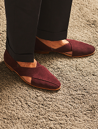 Maroon loafers with gold accents worn by a person on a textured surface