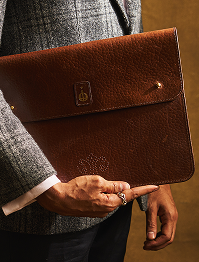 Brown leather briefcase held by a person wearing a gray suit.