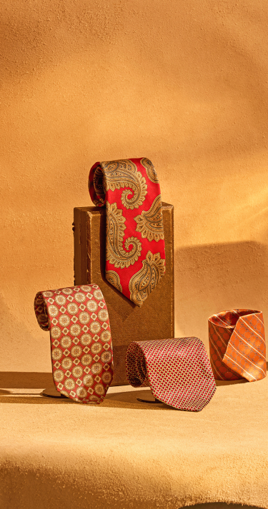 Collection of patterned ties on a textured surface with a warm color palette.