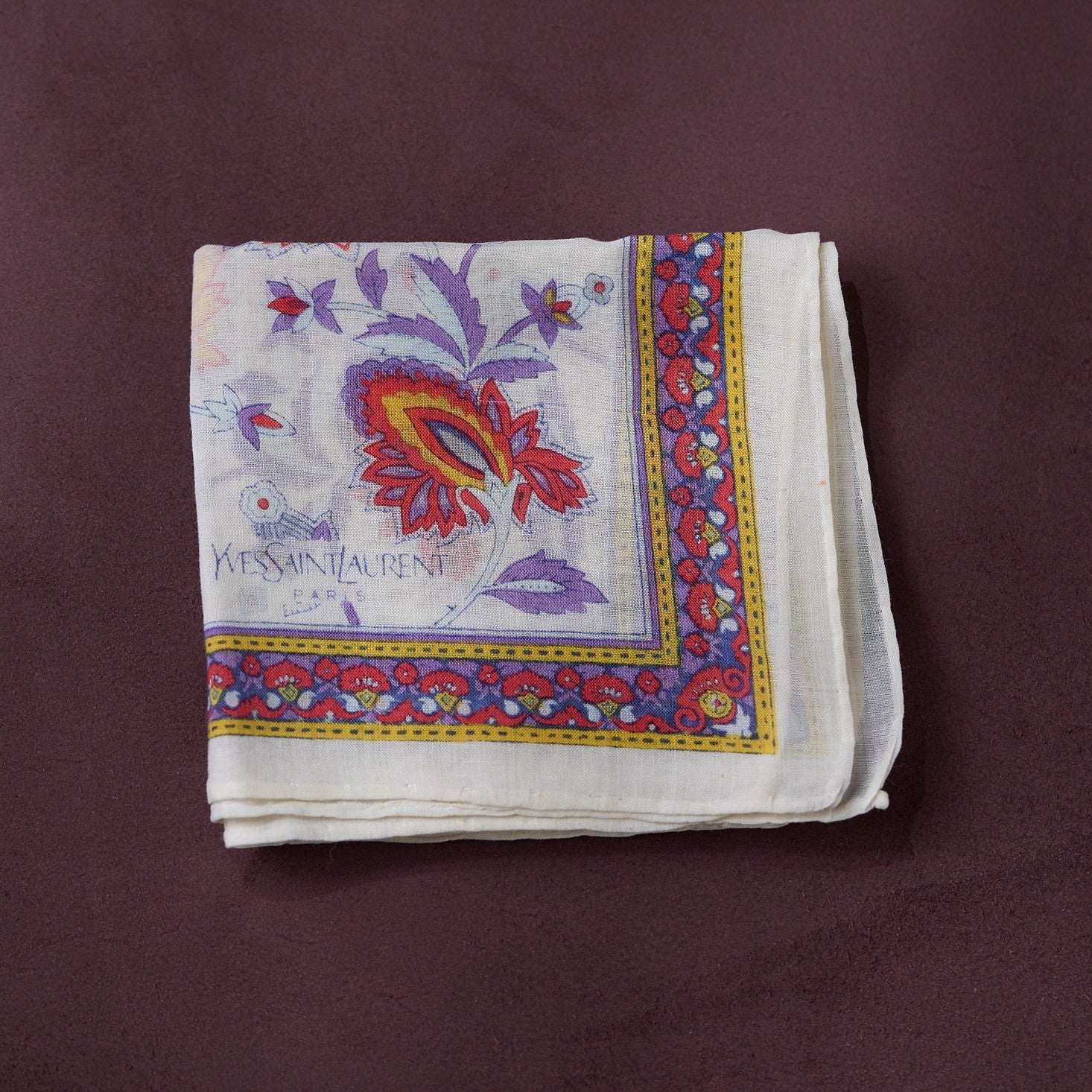 Folded Yves Saint Laurent handkerchief with colorful border on a maroon background