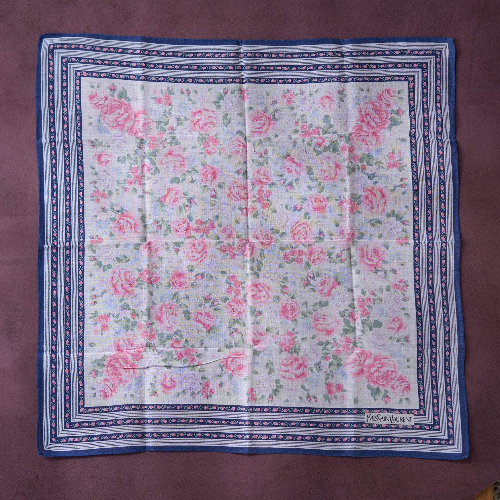 Floral patterned fabric with pink roses on a blue border, displayed on a brown surface.