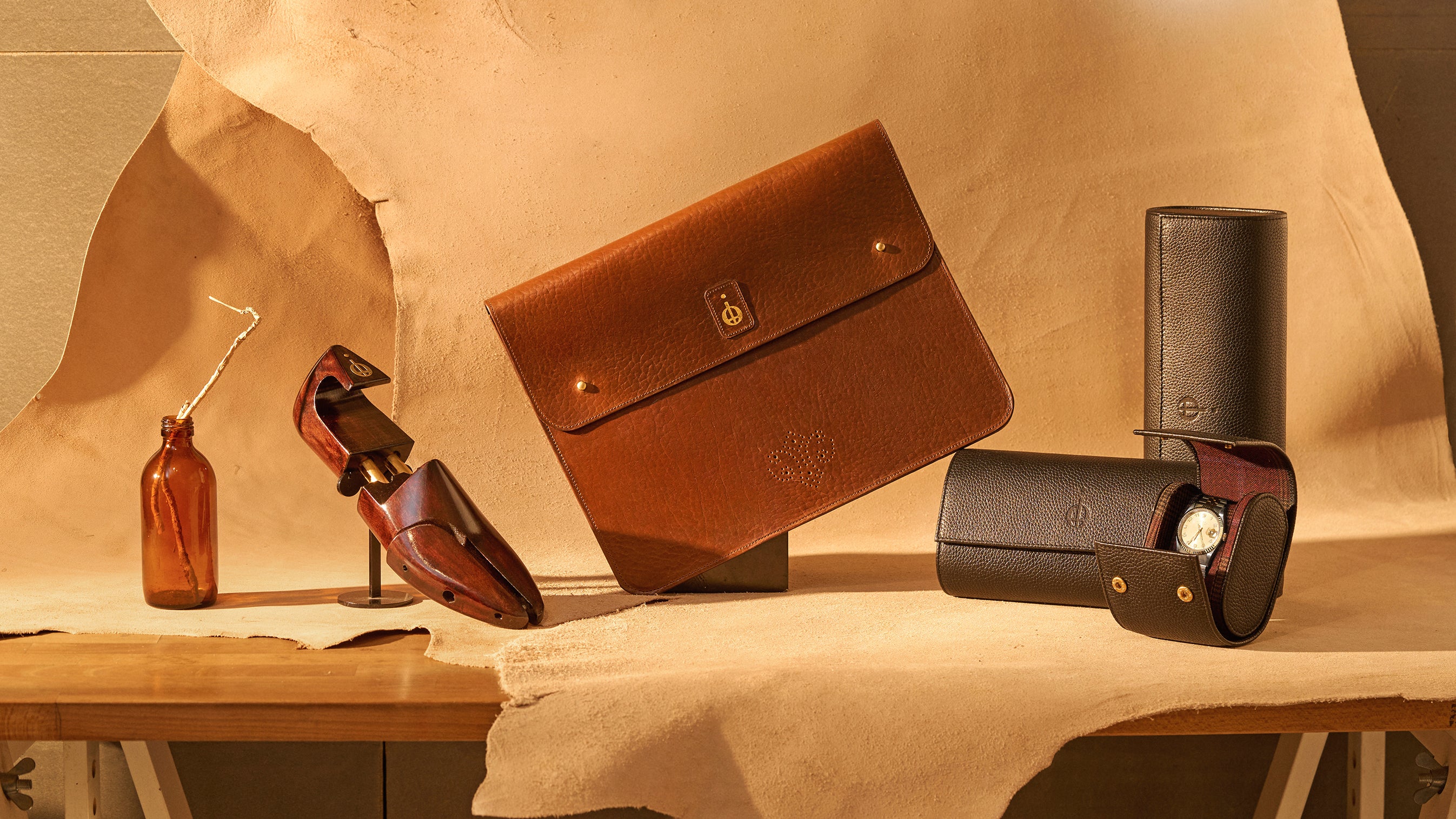 Collection of leather cases and a bottle on a wooden surface with a beige background