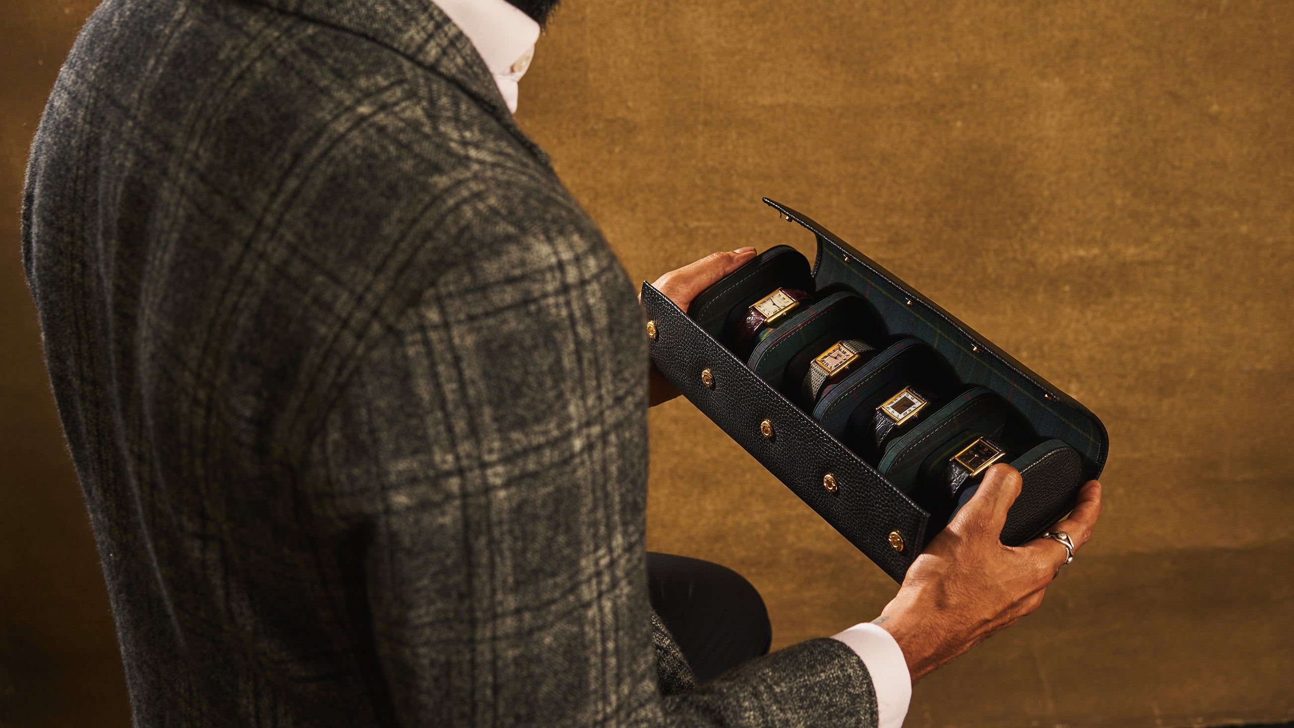 Person holding a black jewelry box with gold rings on a brown background