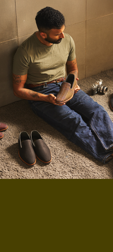 Man sitting on the floor holding a brown shoe, with another shoe beside him.