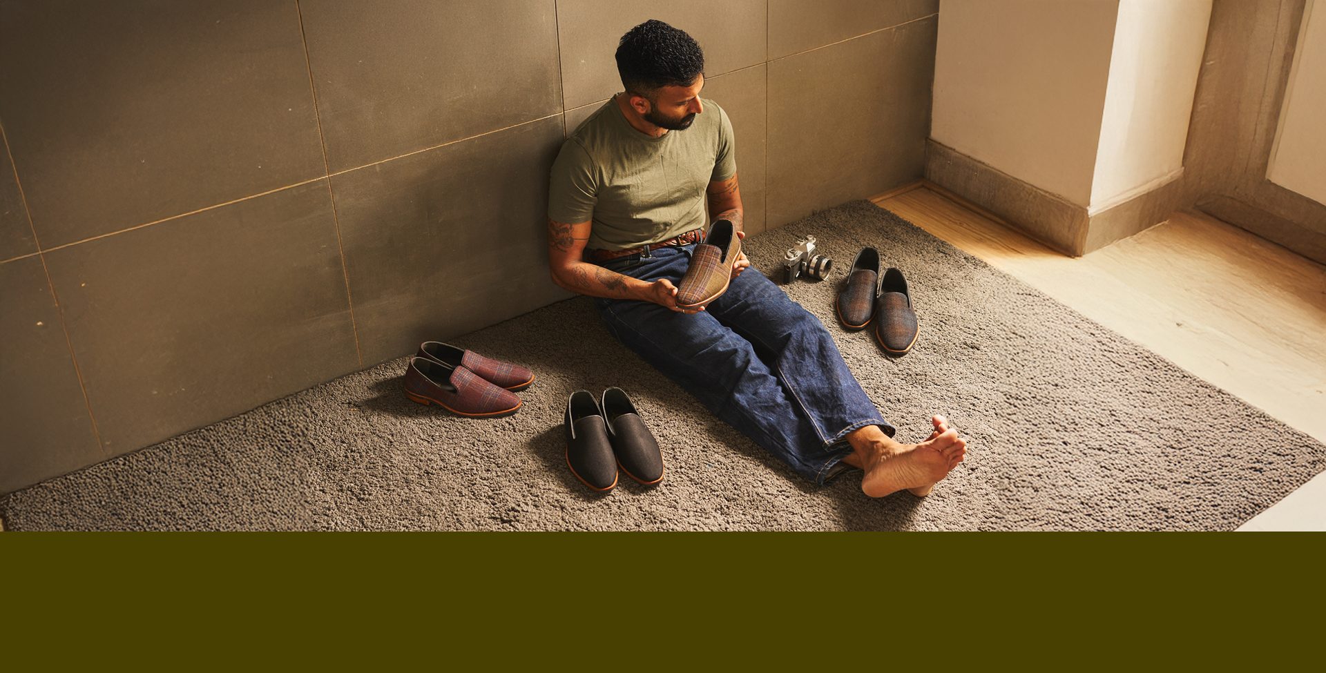 Man sitting on a rug with shoes around him in a room.